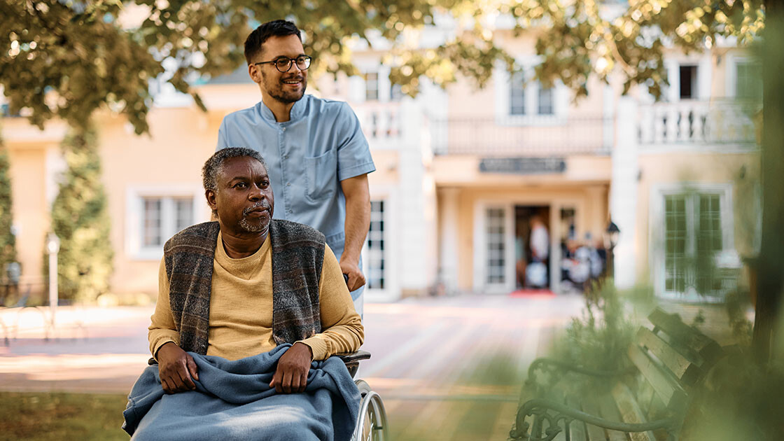 Caregiver supporting an elderly resident in a wheelchair outside a care facility, symbolizing Clarity LTC’s commitment to empowering skilled nursing professionals through better technology.